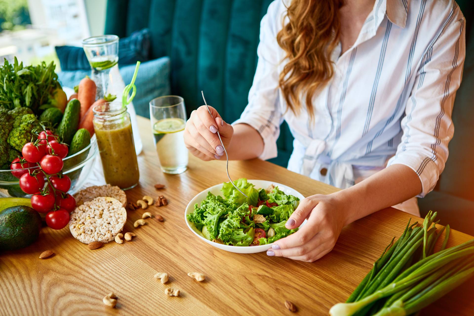 Kvinna som äter sallad vid bord med färska grönsaker